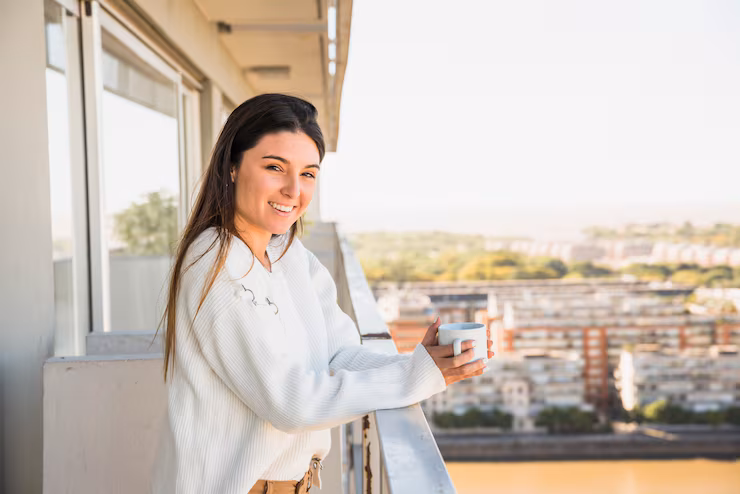 retrato de um sorrindo mulher jovem ficar em sacada segurando branca xicara cafe
